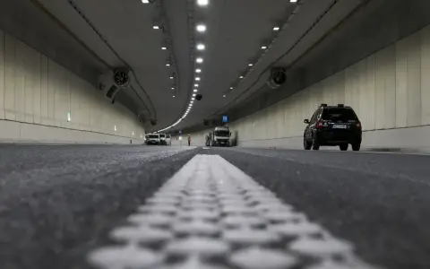 Wnętrze tunelu z samochodami i ciężarówką. Widać wyraźnie jaki odstep w tunelu między pojazdami, oświetlenie i wentylatory.
