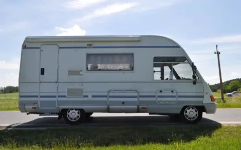 Biały ford galaxy camper z niebieskimi pasami stoi na poboczu drogi. W tle zielone pola i błękitne niebo.