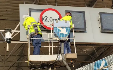 Pracownicy na podnośniku montują znak zakazu 2,0m, pokazując, jak działa e-toll.