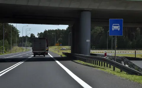 Droga jednojezdniowa pod wiaduktem, z ciężarówką i znakiem informującym o pasie ruchu dla samochodów.
