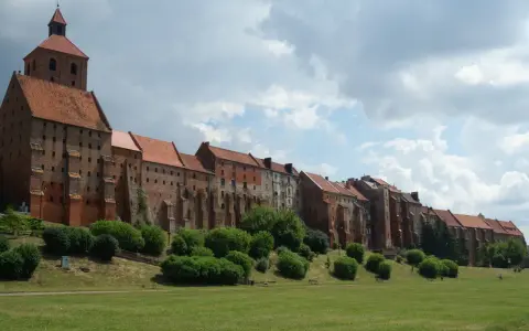 Zabytkowe miasto na trasie Ostróda-Grudziądz z ceglanymi budynkami i wieżą kościelną, otoczone zielenią i parkiem.