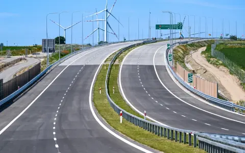 Nowa droga S6 z wiatrakami w tle. Pusta autostrada z zielonym pasem zieleni i barierami.