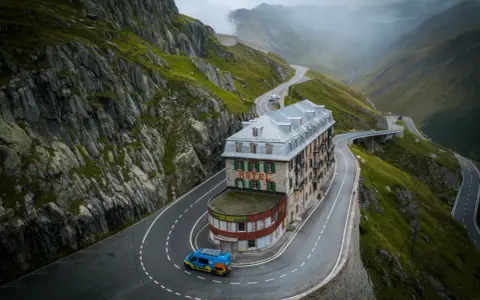 Malowniczy hotel na serpentynach w Alpach, idealny punkt na **grand tour szwajcaria**. Niebieski busik z panelami słonecznymi.