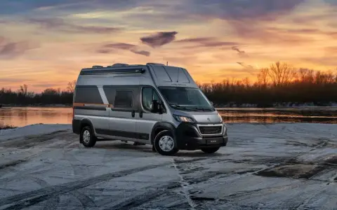 Srebrny kamper Globe-Traveller na tle zachodzącego słońca nad rzeką. Idealny wybór, jeśli zastanawiasz się, jaki kamper dla 2 osób sprawdzi się najlepiej na zimowe wyprawy.