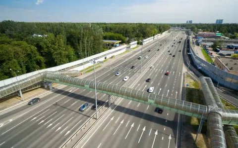 Szerokie drogi w Rosji z zielonym, przeszklonym mostem dla pieszych. Ruch samochodowy na wielopasmowej autostradzie.