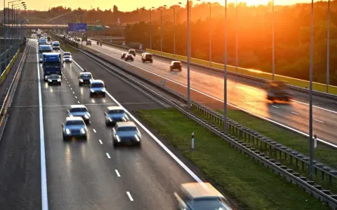 Zachód słońca nad Via Baltica. Samochody i ciężarówki pędzą autostradą w złotym blasku.