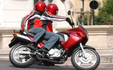 Dwie osoby w kaskach i kurtkach jadą na czerwonym motocyklu. Idealny na pierwsze prawo jazdy na 125.
