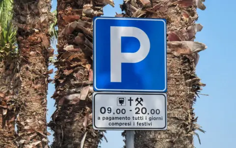 Znaki drogowe we Włoszech: niebieski znak parkingu z literą "P" i tabliczka informująca o płatnym parkingu od 9:00 do 20:00, codziennie, w tym święta.