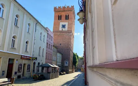 Krzywa wieża w Ząbkowicach Śląskich, ceglana, z zegarem, góruje nad brukowanym rynkiem.