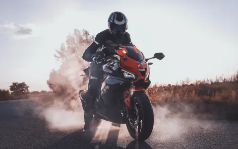 Motocyklista w kasku i kombinezonie na sportowym motocyklu, otoczony dymem. Czy motorem można jeździć po autostradzie? Tak, jeśli spełnia określone wymogi.