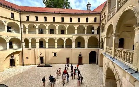Dziedziniec zamku w Ojcowie z arkadowymi krużgankami i grupą turystów.