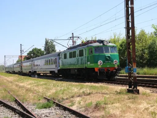 Zielony pociąg EU07-052 z wagonami mija tory w słoneczny dzień. To widok z wieluń trasa.