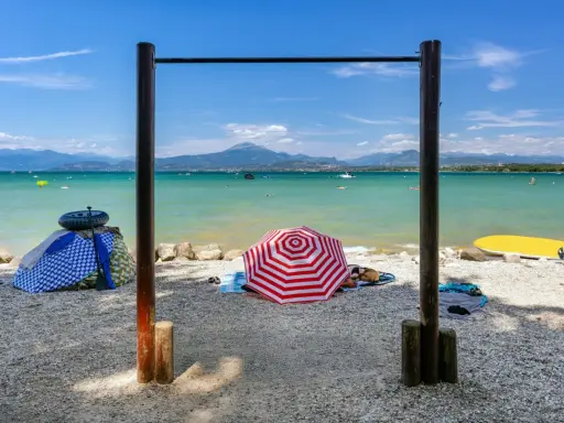 Słoneczne plaże nad jeziorem Garda, z parasolami, leżakami i wodnymi atrakcjami w tle.