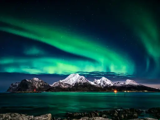 Zielona zorza polarna nad ośnieżonymi górami i morzem. Marzysz, jak dojechać do Norwegii, by zobaczyć to na żywo?