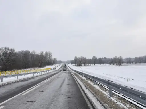 Zimowa trasa, śnieg przy drodze, drzewa bez liści. Nowy tomyśl trasa wita podróżnych.