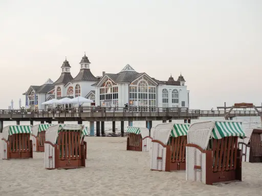 Plaża na wyspie Rugia z charakterystycznymi koszami plażowymi i molo prowadzącym do białego pawilonu.