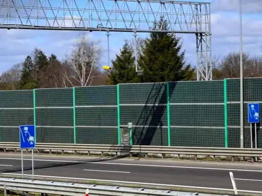 Znak informujący o odcinkowym pomiarze prędkości S3. Za ekranami akustycznymi widać drzewa i niebo.