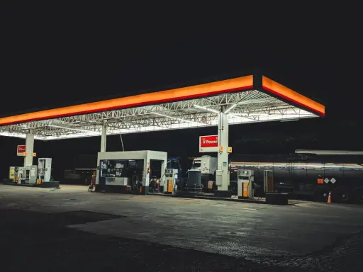 Nocna stacja paliw w Polsce, oświetlona neonami, z dystrybutorami i cysterną.