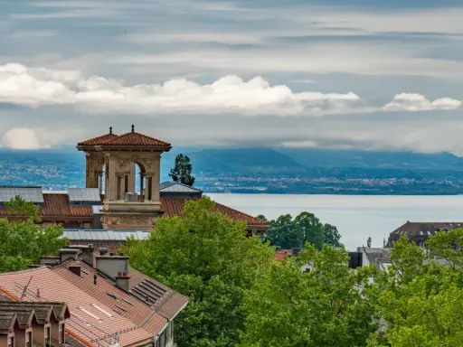 Widok na szwajcarskie miasto nad jeziorem Genewskim, z charakterystyczną wieżą i dachami budynków.
