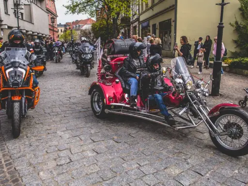 Parada motocykli i trójkołowców na brukowanej ulicy. W tle widzimy ludzi i budynki. To może być początek podróży szwecja motocyklem.