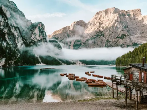 Spokojne jezioro w Dolomitach, Tyrol Włochy, z łodziami przy drewnianym molo i mgłą otulającą góry.