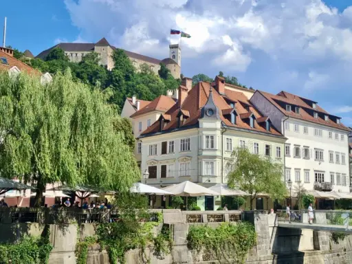 Urokliwy widok na rzekę i zabytkowe kamienice w Słowenii, Lublana. W tle widać zamek na wzgórzu.