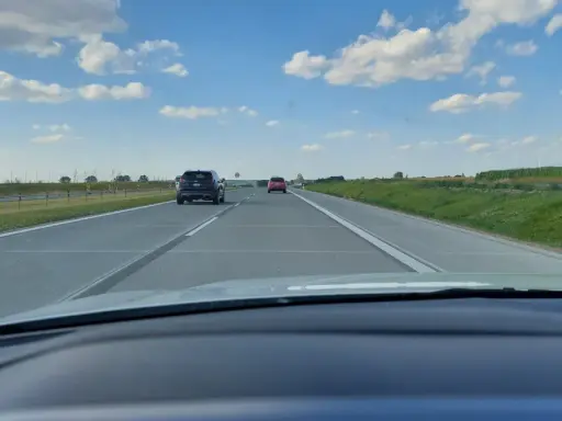 Jadąc na S7, widzimy pola i chmury. Samochody poruszają się po pustej drodze.