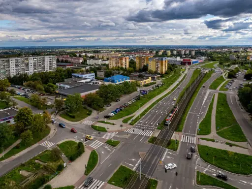 Widok z lotu ptaka na ruchliwe skrzyżowanie w Gdańsku Chełmie, z tramwajem, samochodami i budynkami mieszkalnymi w tle.