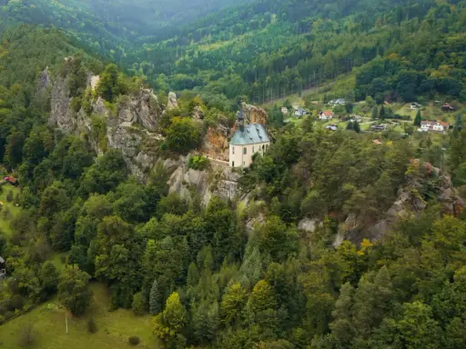 Malowniczy kościółek na skale, otoczony lasami, to jedno z **ciekawych miejsc w Czechach**. W oddali widać domki w dolinie.