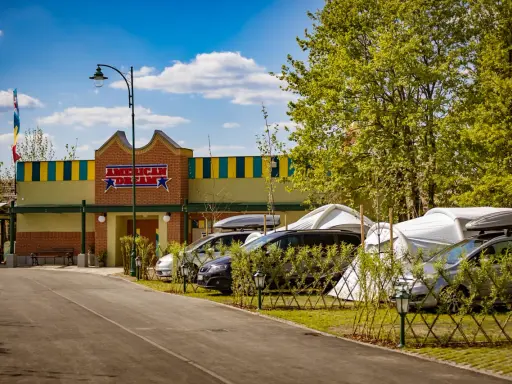 Zator Energylandia trasa: parking z samochodami i namiotami pod budynkiem "American Dream" w słoneczny dzień.