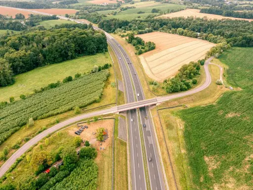 Nowa sól trasa przecina zielone pola i lasy, łącząc odległe zakątki. Widok z lotu ptaka ukazuje drogę, most i samochody w ruchu.