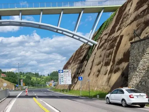 Biały samochód na granicy Polski, przygotowuje się do podróży do Danii samochodem. Nad drogą wznosi się imponujący most.