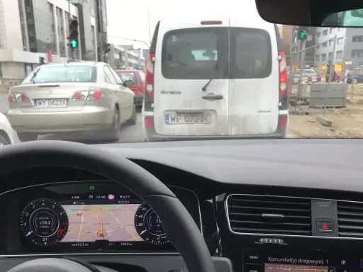 Utrudnienia na drodze, korek przed budową. Samochody stoją w deszczu, nawigacja pokazuje objazd.