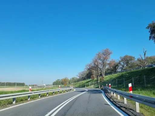 Słupki na autostradzie wyznaczają zakręt drogi. Jasne niebo i zielone pobocze tworzą malowniczy krajobraz.
