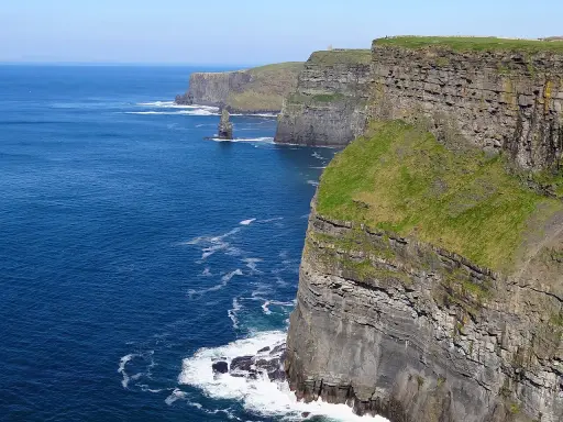 Majestatyczne klify Irlandii wznoszą się nad błękitnym oceanem. Zielone zbocza kontrastują z szarymi skałami, tworząc zapierający dech w piersiach krajobraz.