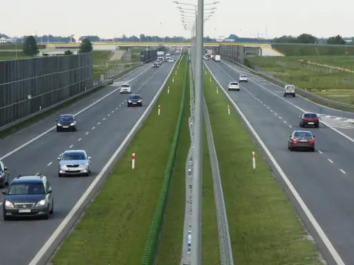 Różne rodzaje dróg: autostrada z pasami ruchu, barierkami i ekranami akustycznymi. Samochody poruszają się po jezdni.