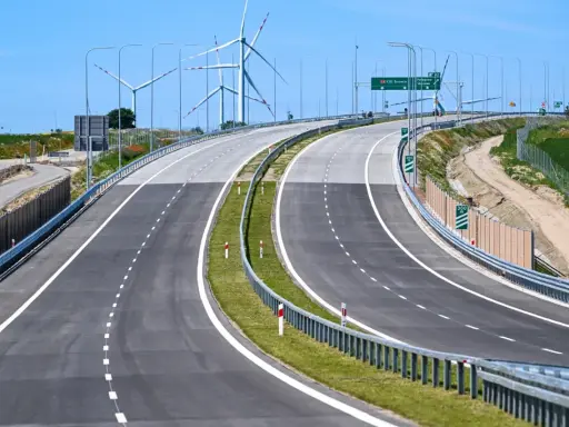 Nowa droga S6 z wiatrakami w tle. Pusta autostrada z zielonym pasem zieleni i barierami.