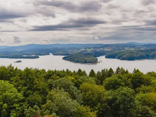Widok na Jezioro Solińskie zalesione wzgórza, w oddali widać zabudowania. Odległość Sanok Polańczyk.