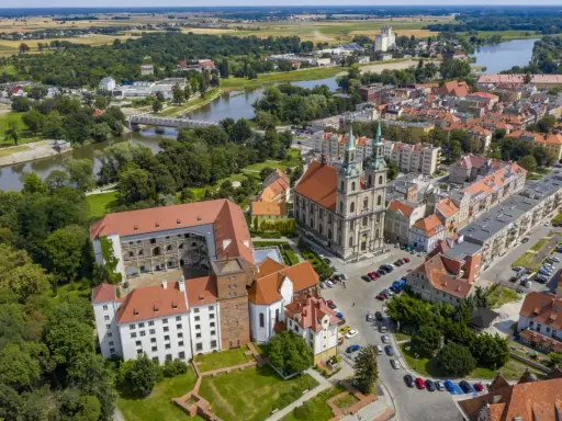 Zamek Piastów Śląskich w otoczeniu miasta i rzeki. Zabytkowa budowla z czerwonymi dachami, obok katedra z zielonymi wieżami.
