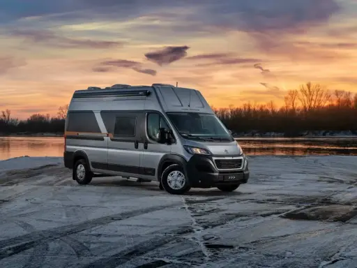 Srebrny kamper Globe-Traveller na tle zachodzącego słońca nad rzeką. Idealny wybór, jeśli zastanawiasz się, jaki kamper dla 2 osób sprawdzi się najlepiej na zimowe wyprawy.