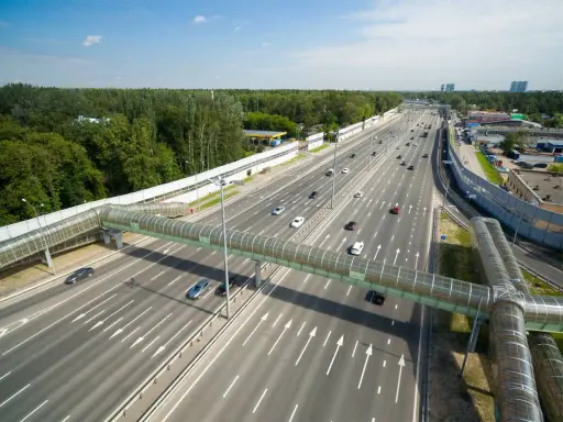 Szerokie drogi w Rosji z zielonym, przeszklonym mostem dla pieszych. Ruch samochodowy na wielopasmowej autostradzie.