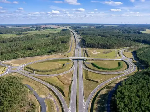 Węzeł drogowy na trasie Poznań-Kołobrzeg. Nowoczesna infrastruktura drogowa otoczona lasami i polami.