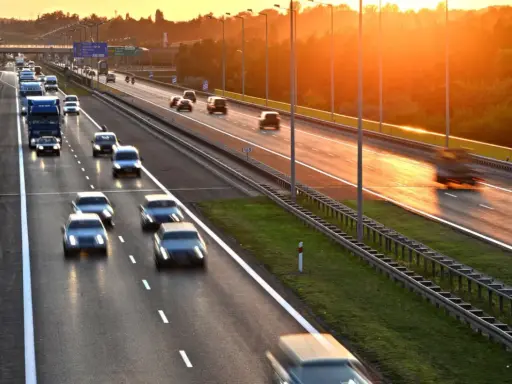 Zachód słońca nad Via Baltica. Samochody i ciężarówki pędzą autostradą w złotym blasku.