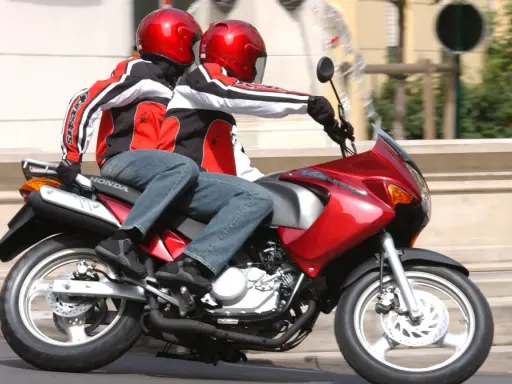Dwie osoby w kaskach i kurtkach jadą na czerwonym motocyklu. Idealny na pierwsze prawo jazdy na 125.