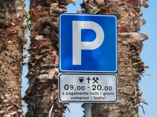 Znaki drogowe we Włoszech: niebieski znak parkingu z literą "P" i tabliczka informująca o płatnym parkingu od 9:00 do 20:00, codziennie, w tym święta.