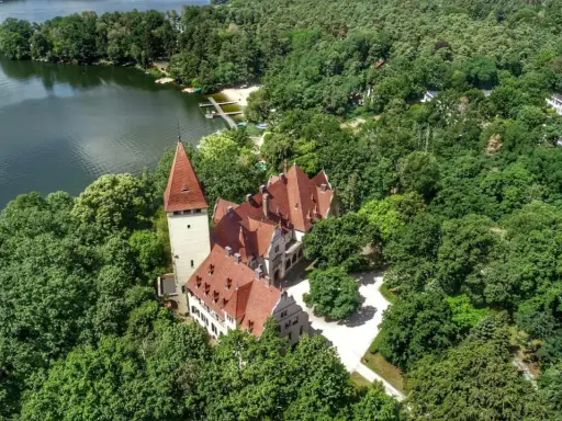 Zamek w Lubniewicach, otoczony bujną zielenią, malowniczo położony nad jeziorem.