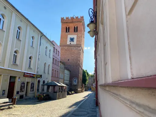 Krzywa wieża w Ząbkowicach Śląskich, ceglana, z zegarem, góruje nad brukowanym rynkiem.
