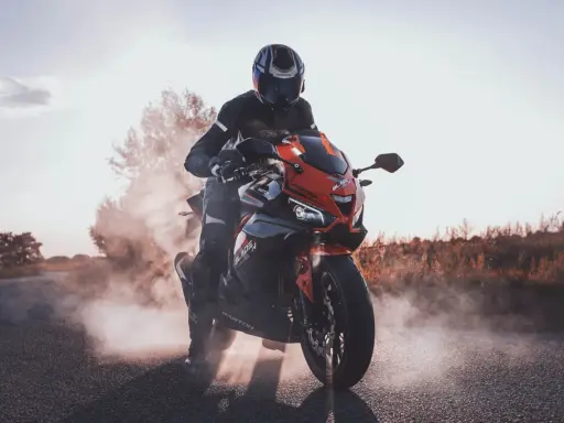 Motocyklista w kasku i kombinezonie na sportowym motocyklu, otoczony dymem. Czy motorem można jeździć po autostradzie? Tak, jeśli spełnia określone wymogi.