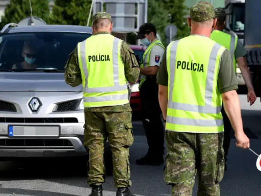 Policjanci w kamizelkach odblaskowych kierują ruchem podczas przejazdu przez Słowację. Kierowca w masce zatrzymuje się do kontroli.
