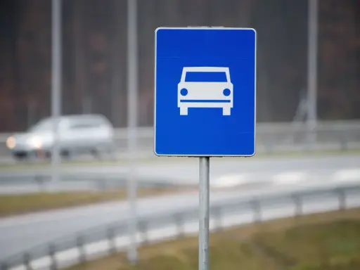 Znak drogowy szybkiego ruchu z symbolem samochodu. W tle widać rozmazany pojazd na drodze.